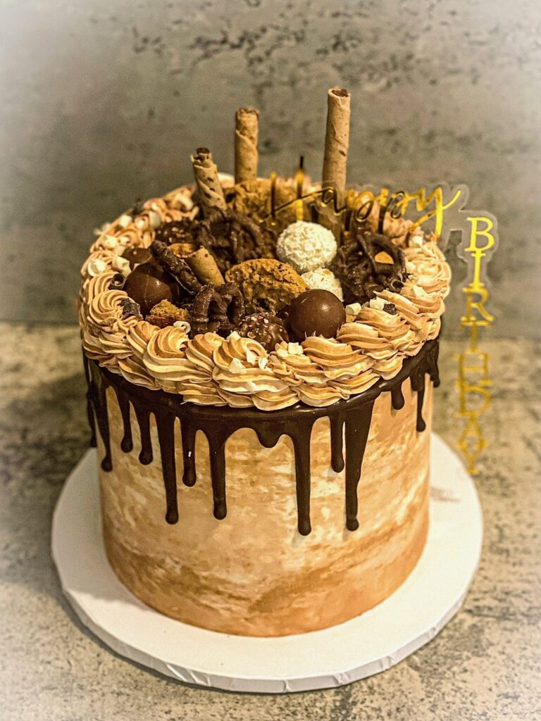 Loaded chocolate drip birthday cake with vanilla buttercream, chocolate ganache drip, cookies, and assorted chocolate toppings created by Luxe Layers Cakery in Miami Florida.