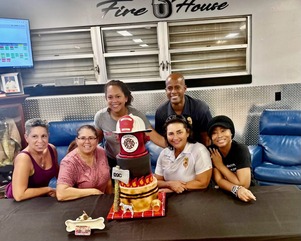Luxe Layers Cakery owner Lynette Stubbs with Chief Yoly Alvarez and City of Miami Fire Department staff celebrating retirement with custom firefighter tribute cake in Miami Florida.