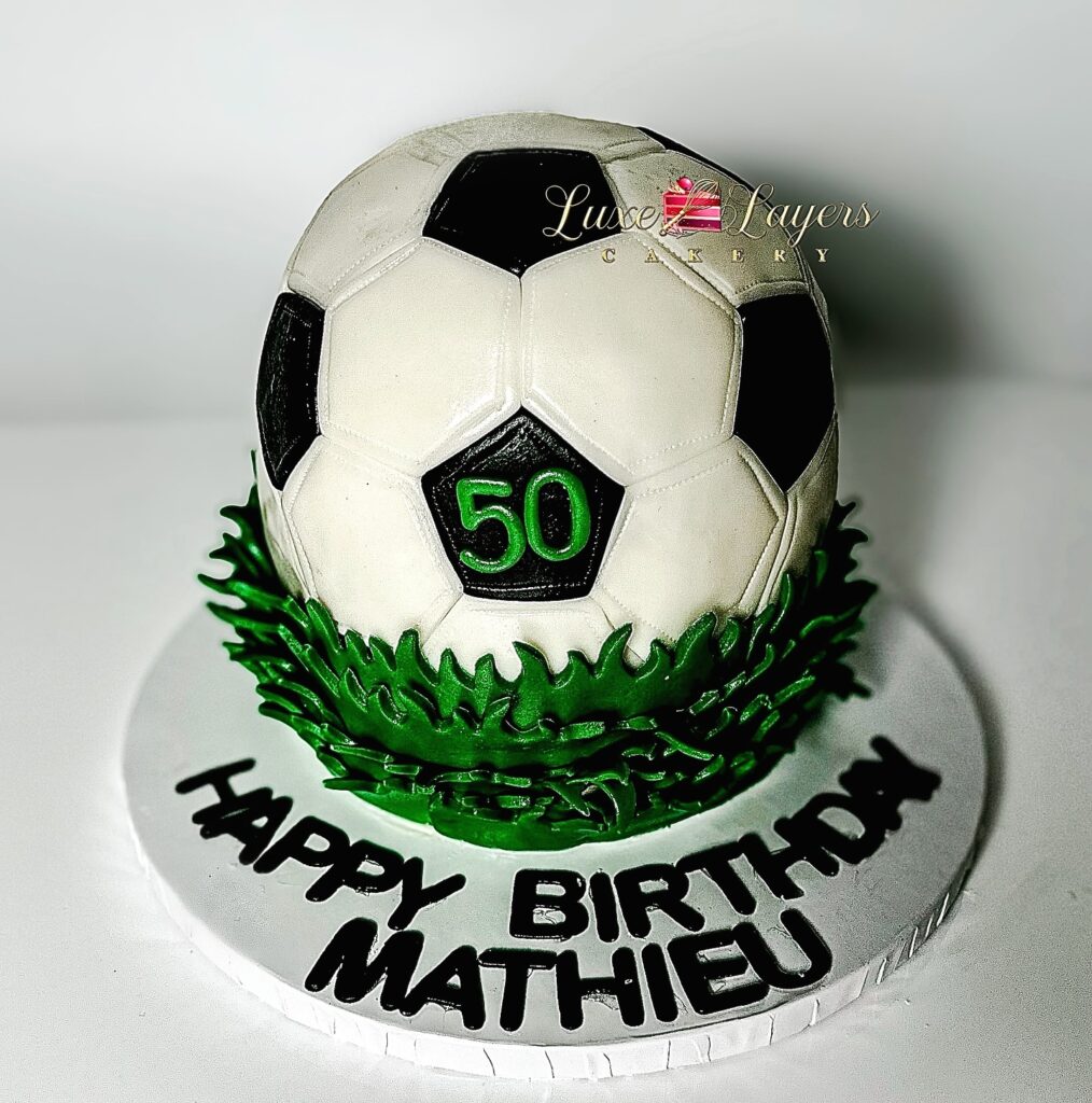 Sculpted 3D soccer ball 50th birthday cake with black and white fondant paneling, green grass base, and custom name lettering, made by Luxe Layers Cakery in Miami, Florida