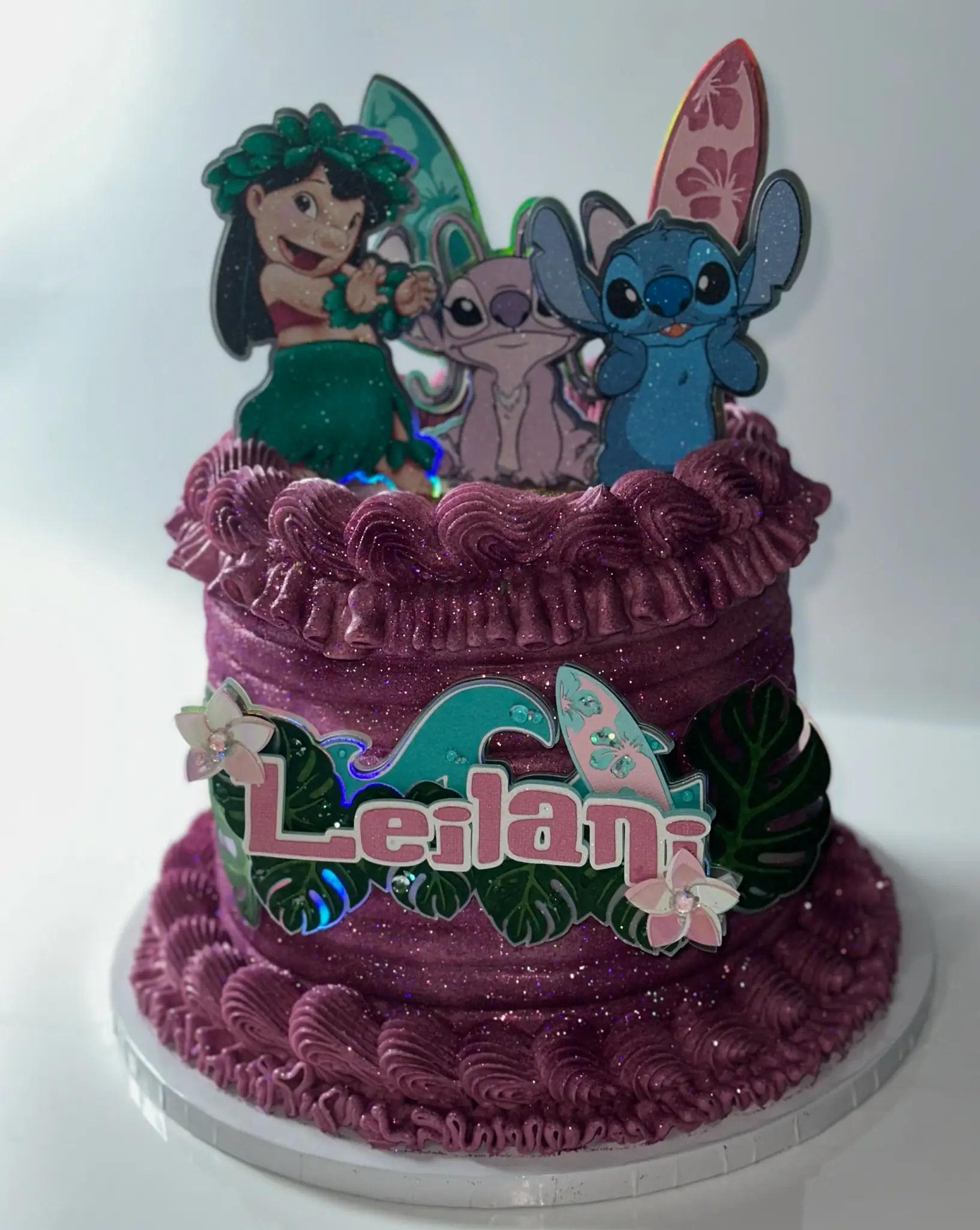 Purple and teal Lilo and Stitch 8th birthday cake with ruffled buttercream piping, tropical leaves, surfboard accents, and shimmer finish — kids birthday cakes Miami by Luxe Layers Cakery