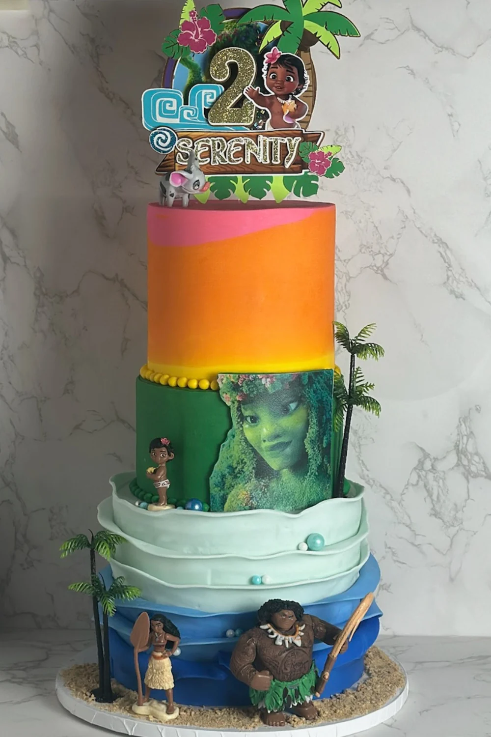 Tiered orange, teal, and blue Moana-themed 2nd birthday cake with ocean wave textures, palm trees, sand base detail, and tropical character accents — kids birthday cakes Miami by Luxe Layers Cakery