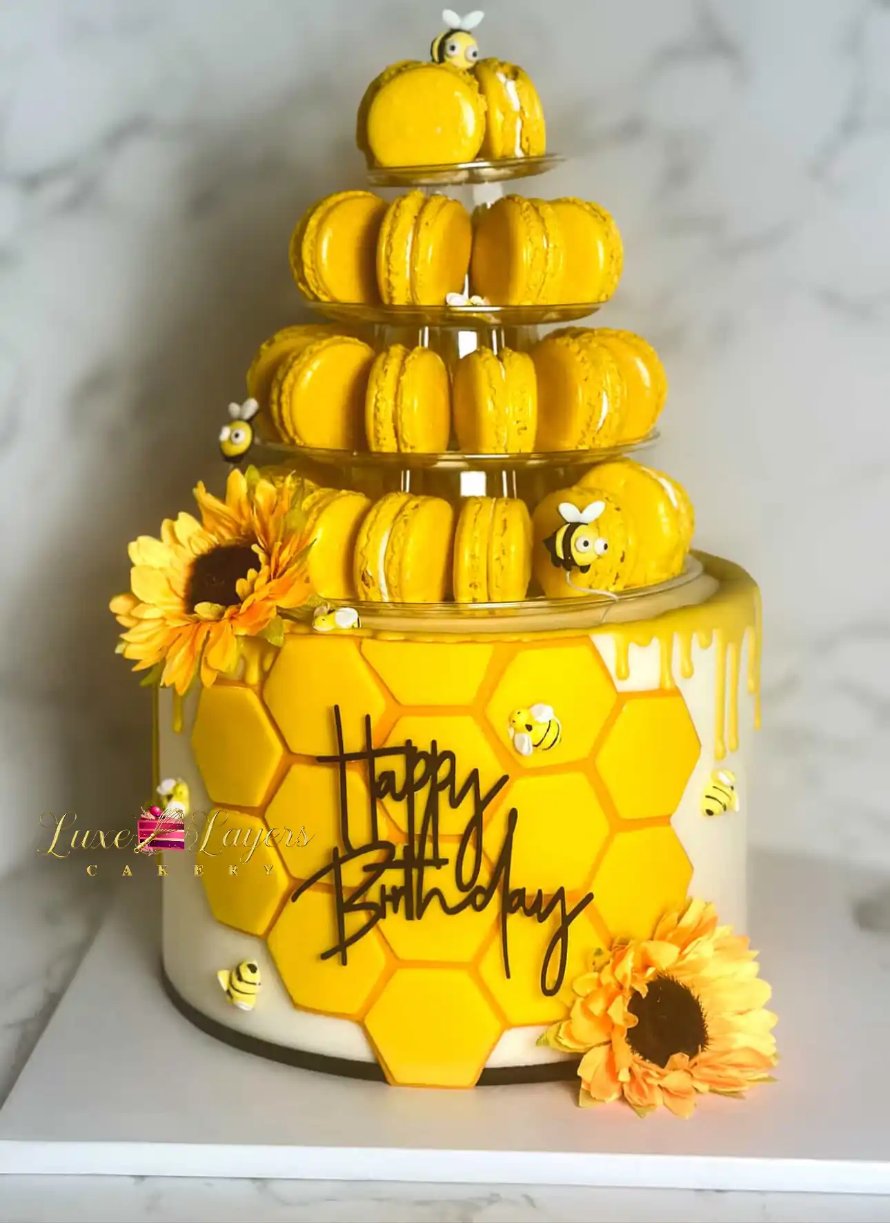 Four-tier honeycomb drip cake topped with yellow macarons and sugar bees, custom birthday cake by Luxe Layers Cakery