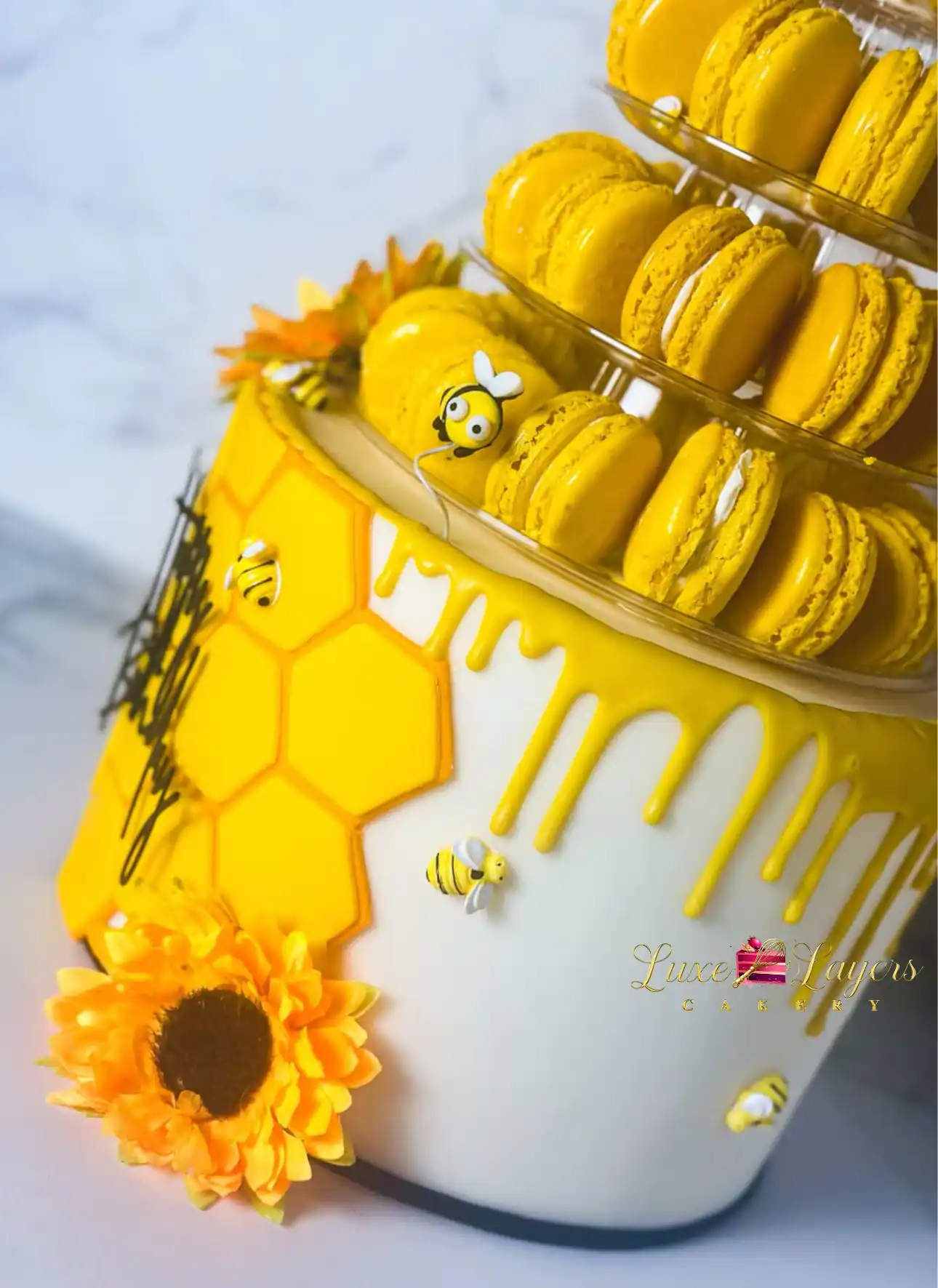 Honeycomb and macaron tower birthday cake with sunflowers on marble backdrop, Luxe Layers Cakery custom design