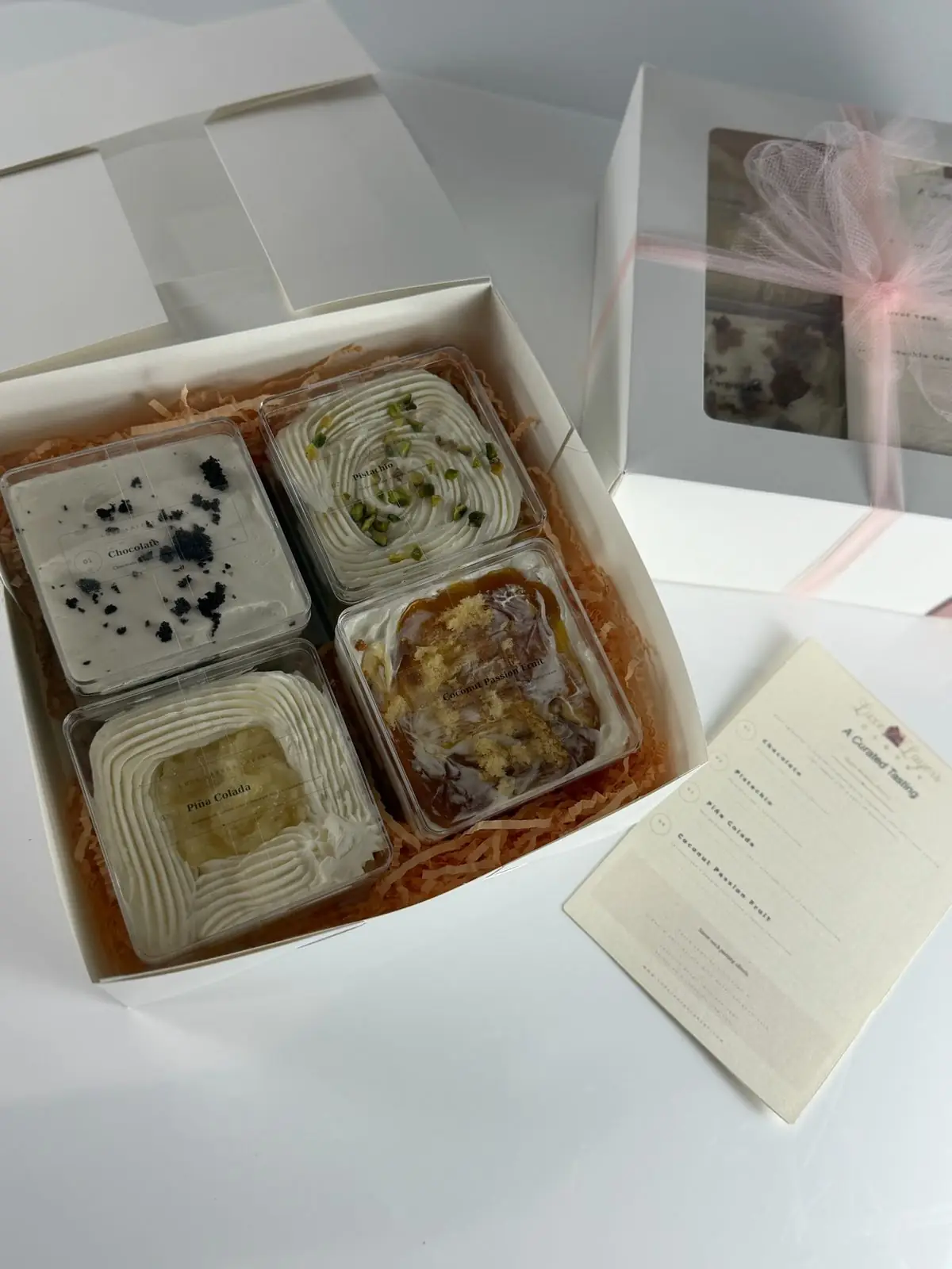 Top view of an open cake taster box with chocolate, pistachio, piña colada and coconut passion fruit containers in crinkle paper