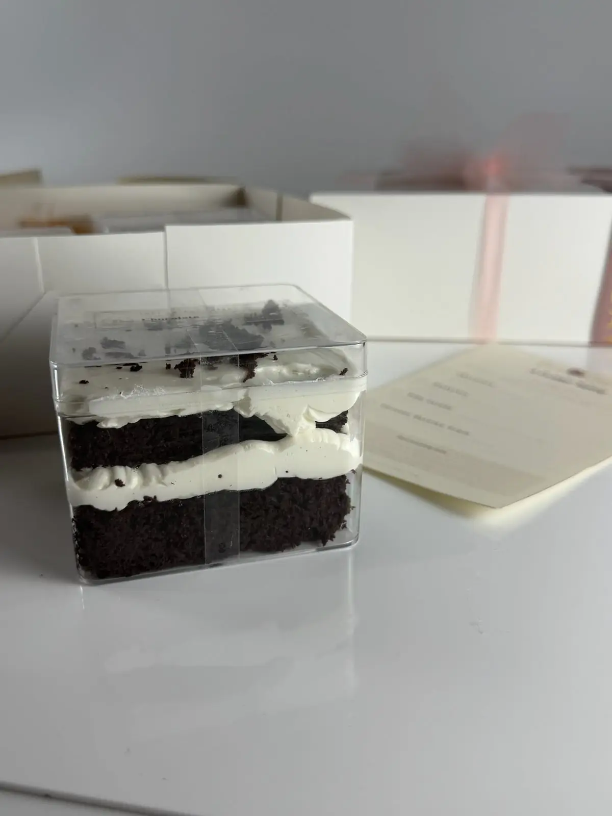 Chocolate cake taster container with two layers of dark chocolate cake and white frosting topped with chocolate cake crumbs