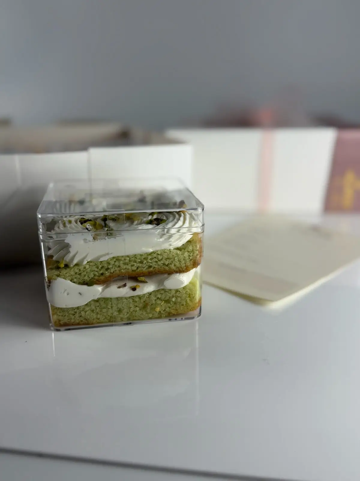 Pistachio cake taster container with two layers of green pistachio cake, white frosting and chopped pistachios on top